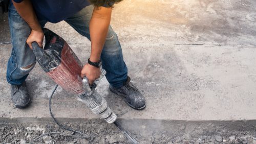 Male,Worker,Repairing,Driveway,Surface,With,Jackhammer,,Digging,And,Drilling