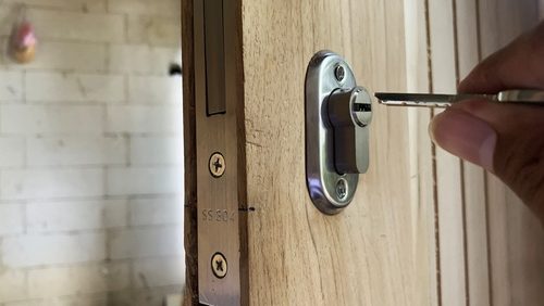 Hand,Inserting,Key,Into,Modern,Door,Lock,Cylinder,On,Wooden