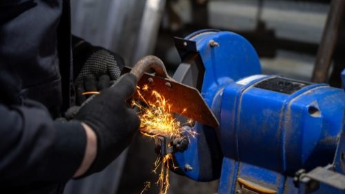 Worker,Sharpening,Hoe,And,Garden,Tools,On,Bench,Grinder,,Pressing