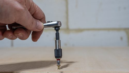 Man,Tightening,A,Brass,Screw,Into,A,Plywood,Workbench,Using
